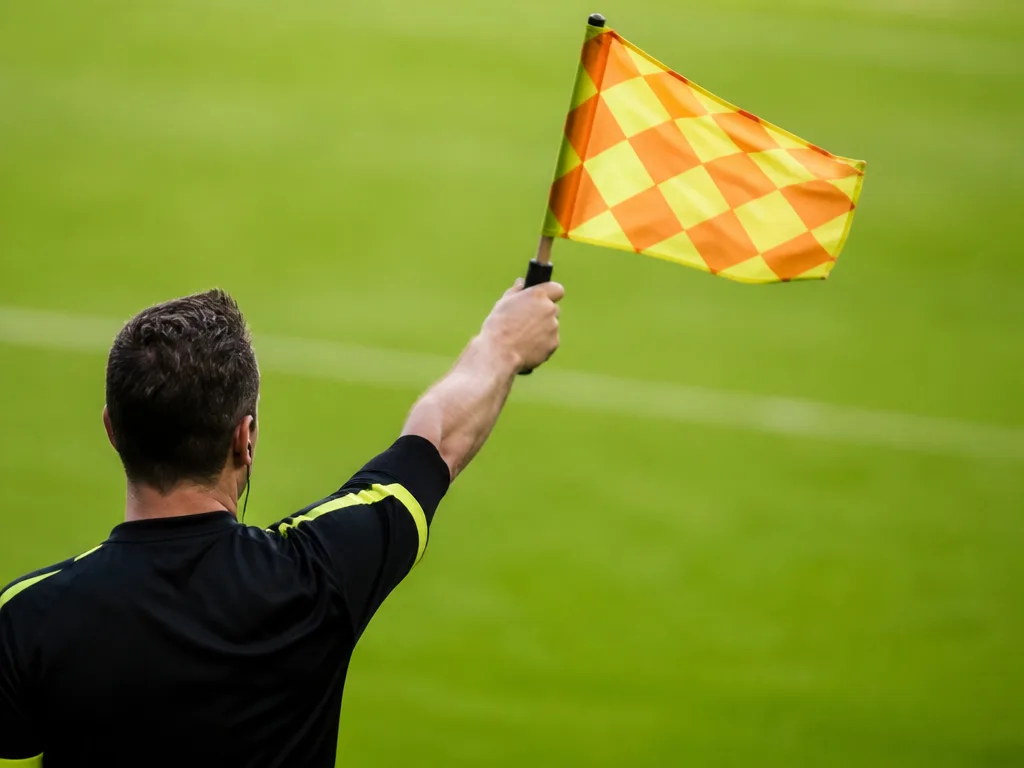 Assisterande domare håller upp flaggan för offside längs sidlinjen under en fotbollsmatch